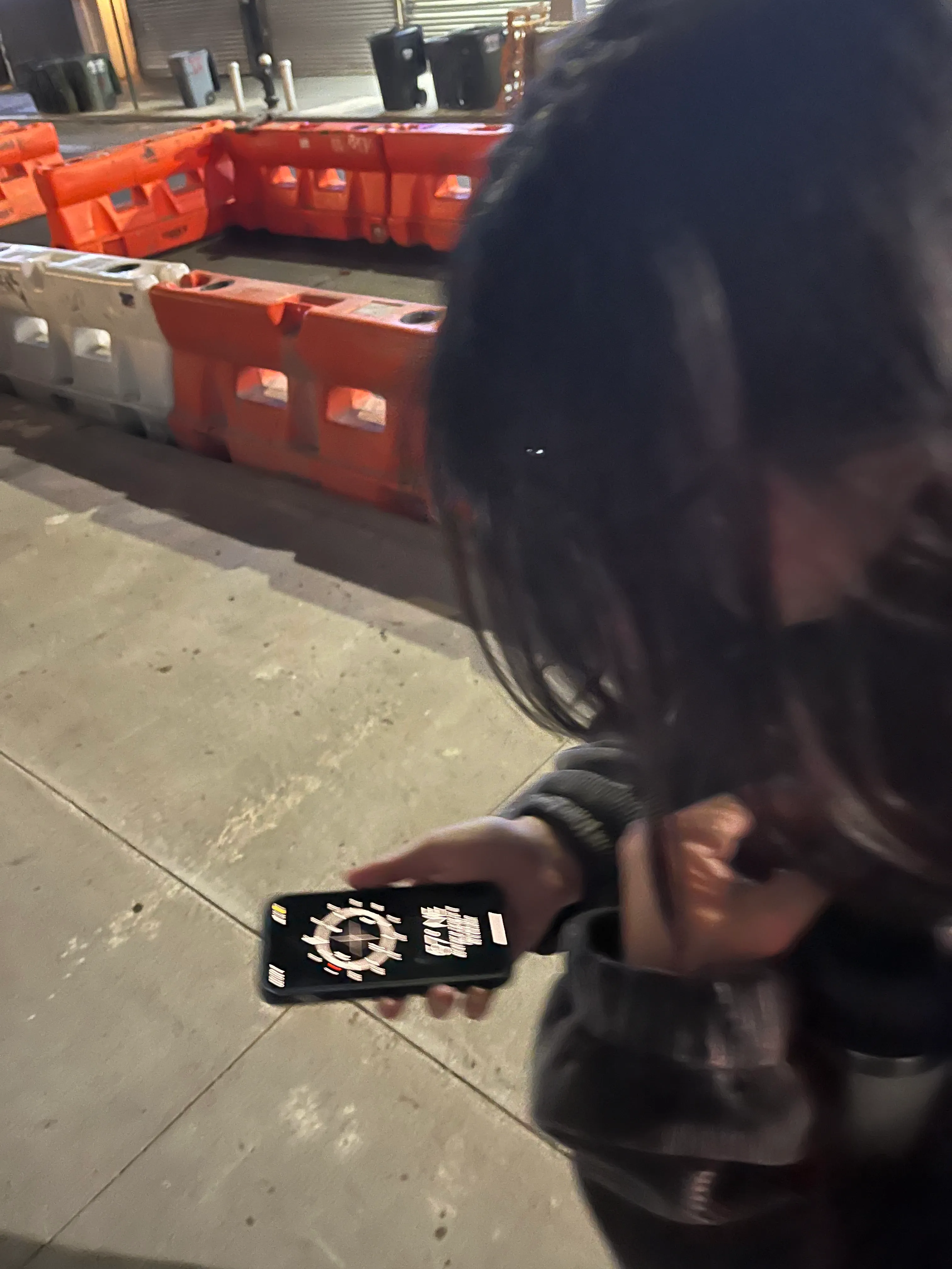 A person checking a phone beside orange construction barriers at night
